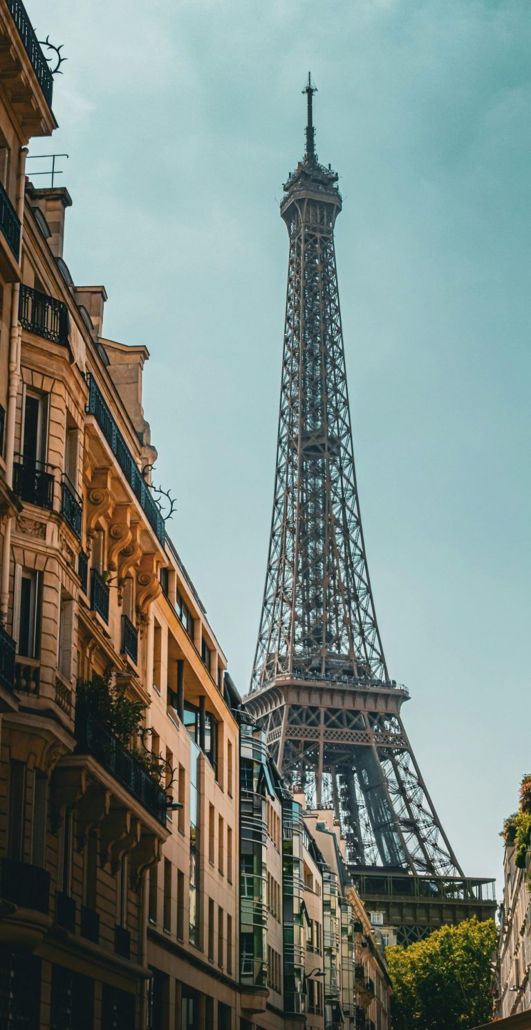Iconic Eiffel Tower view from a Parisian street, highlighting classic French architecture under a clear sky.