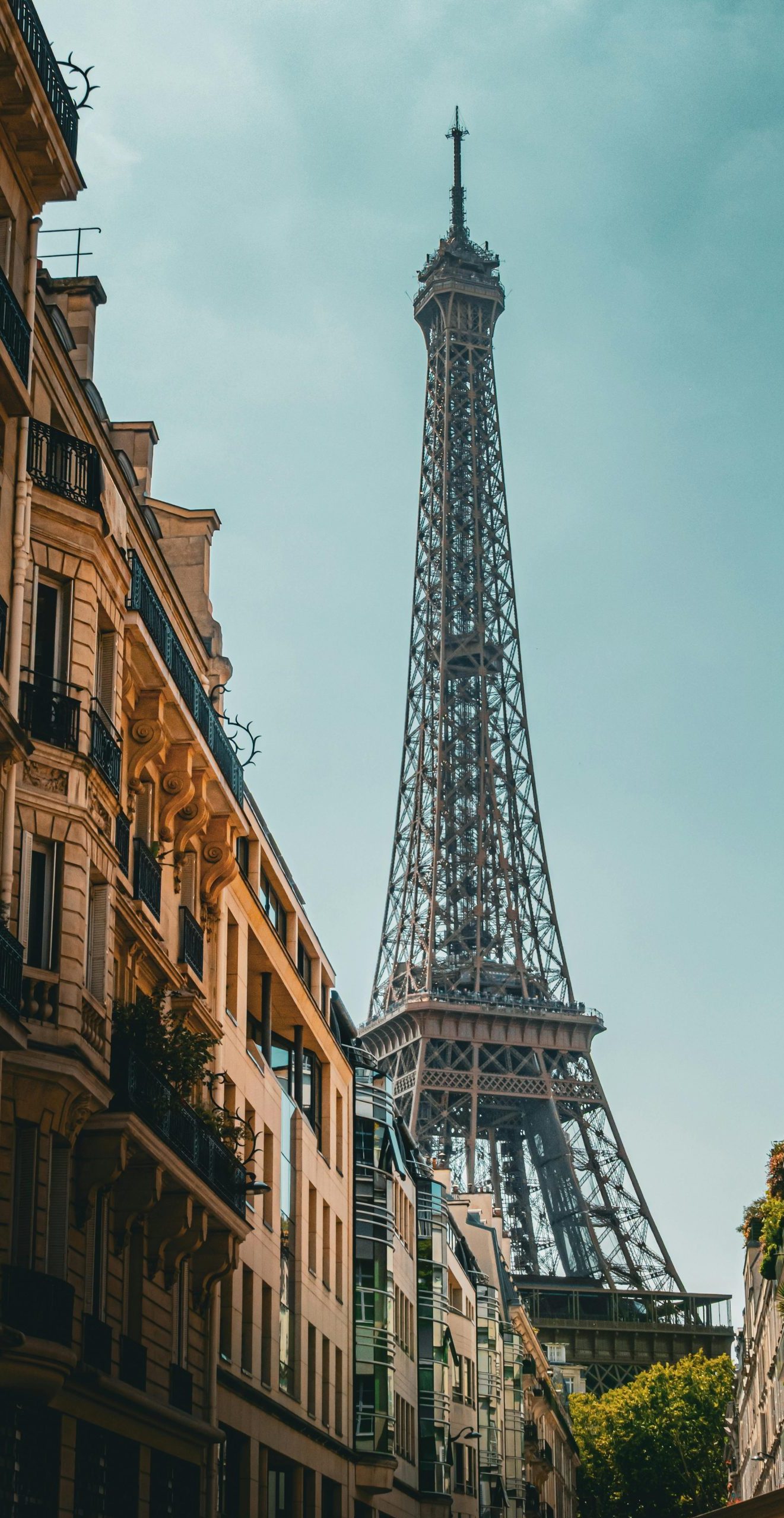 Iconic Eiffel Tower view from a Parisian street, highlighting classic French architecture under a clear sky.